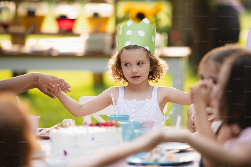 Vorderansicht eines kleinen Mädchens mit Kuchen, das im Sommer im Freien im Garten Geburtstag feiert, Partykonzept.
