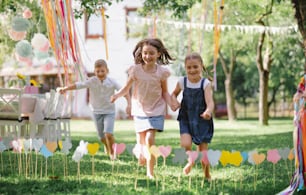 Small children outdoors in garden in summer, running when playing. A celebration concept.