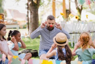 Un homme avec de jeunes enfants assis par terre à l’extérieur dans le jardin en été, en train de jouer.