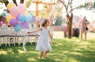 Portrait of happy small girl playing with balloons outdoors on garden party in summer.