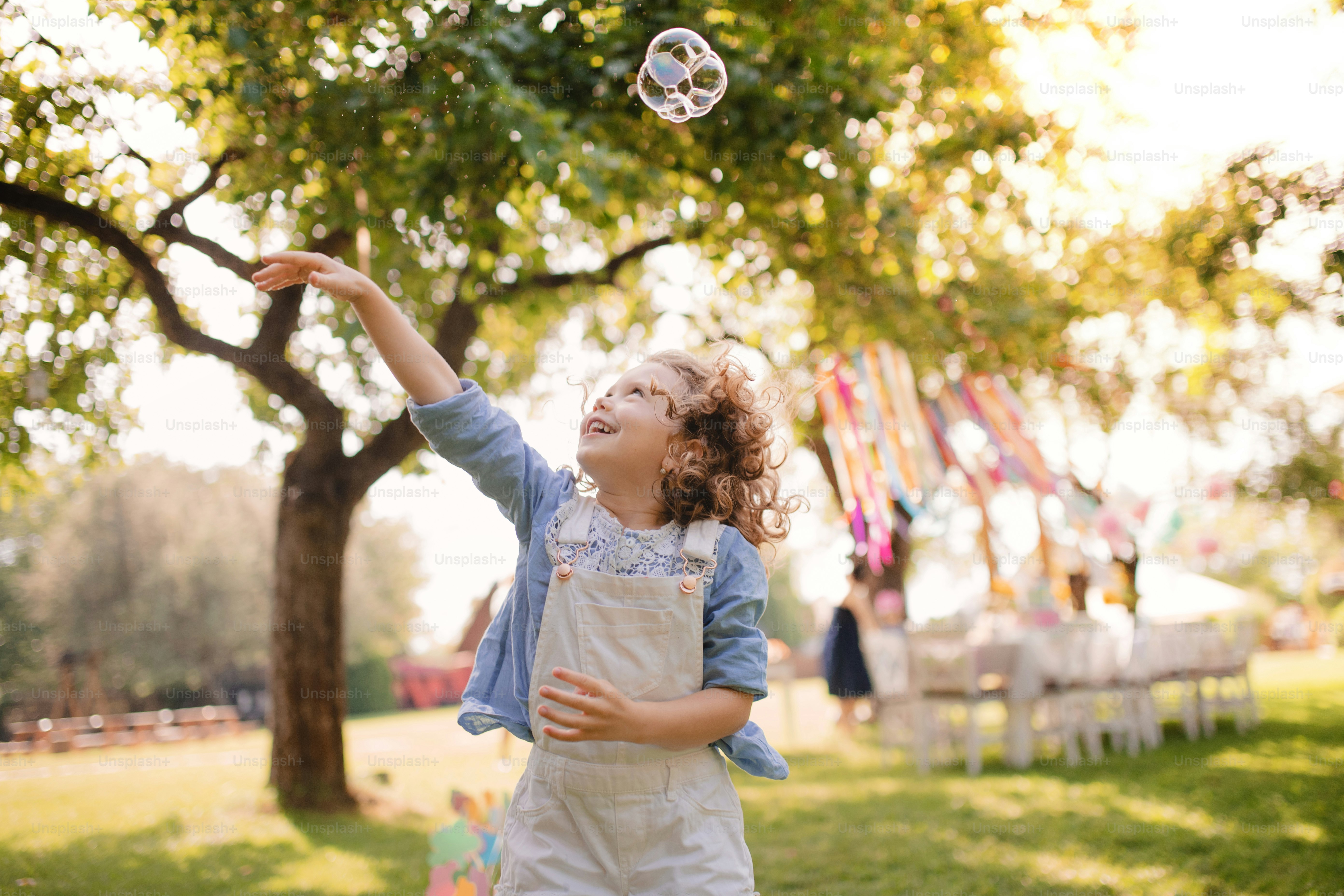 Portrait of happy small girl playing with bubbles outdoors on garden party in summer