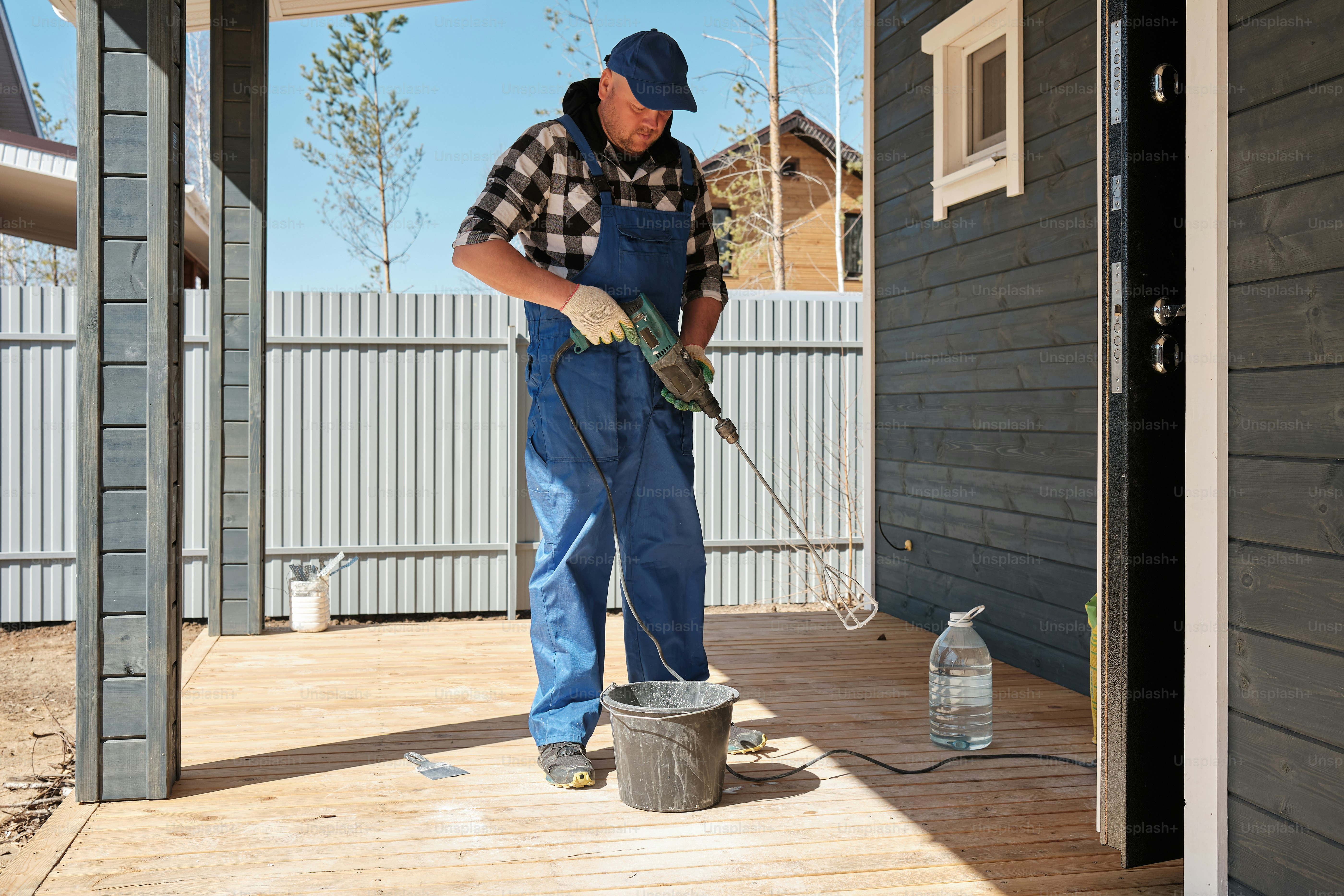 A man in overalls and a hat is cleaning a porch photo – Building Image ...