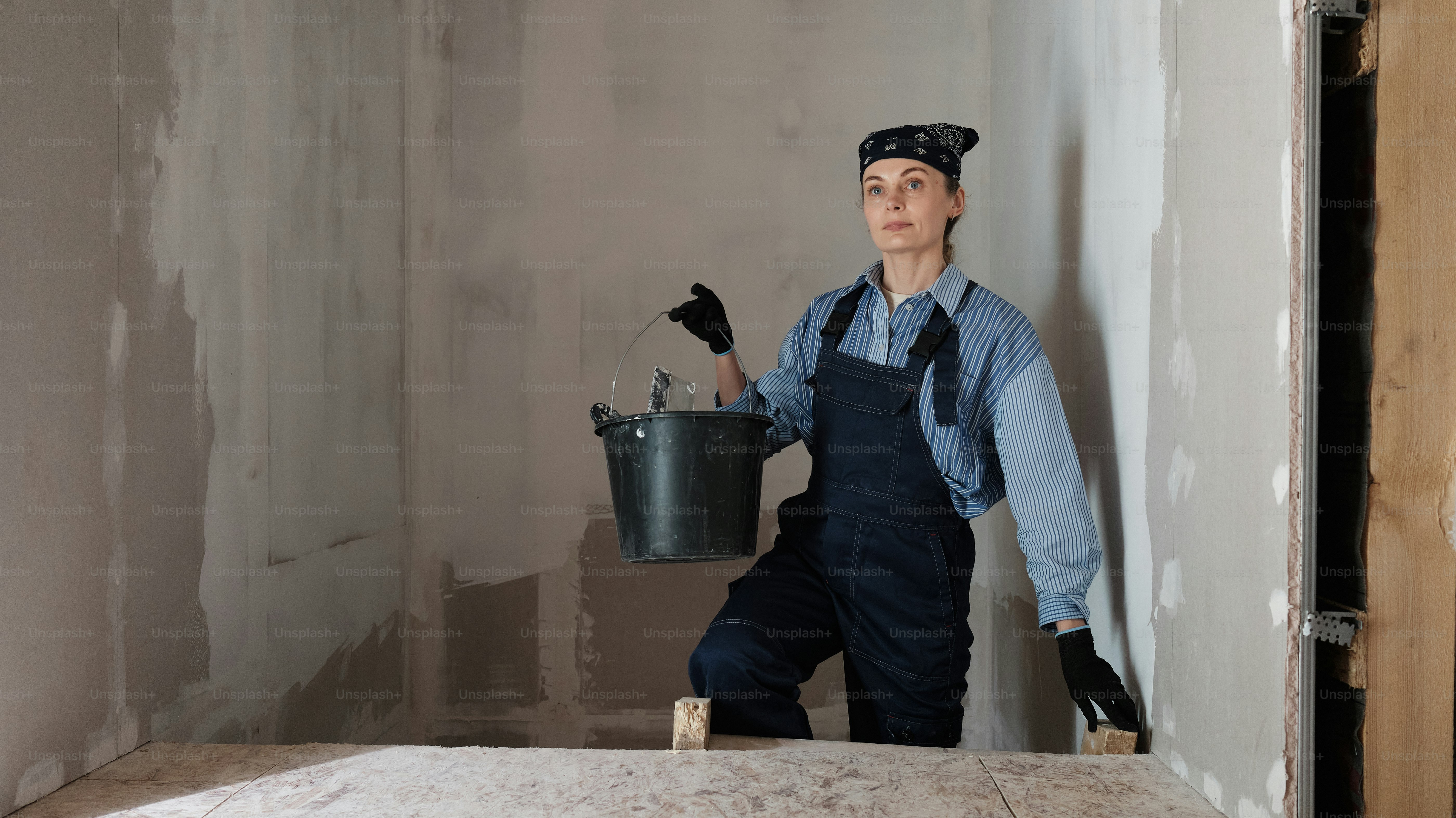 a woman climbs the stairs in a house under construction with plaster mix in her hands
