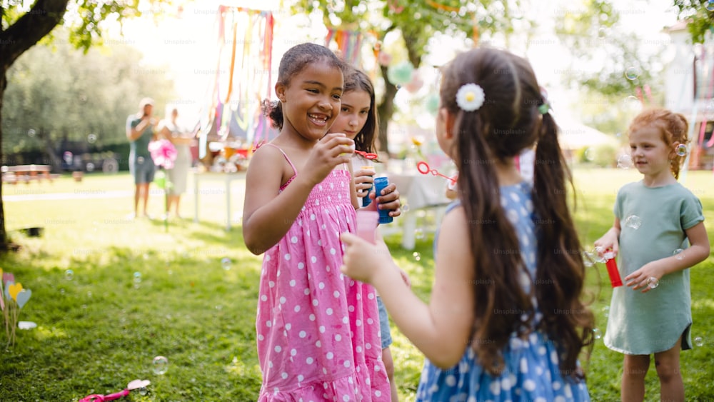 Bambini piccoli in piedi all'aperto in giardino in estate, giocando. Un concetto di celebrazione.