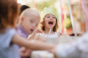 Small children sitting at the table outdoors on garden party in summer, talking.