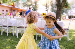 Small girls dancing outdoors in garden in summer, a birthday celebration concept.