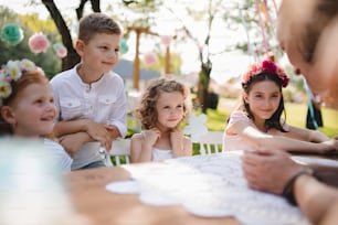 Les petits enfants assis à la table à l’extérieur lors d’une garden-party en été, discutent.