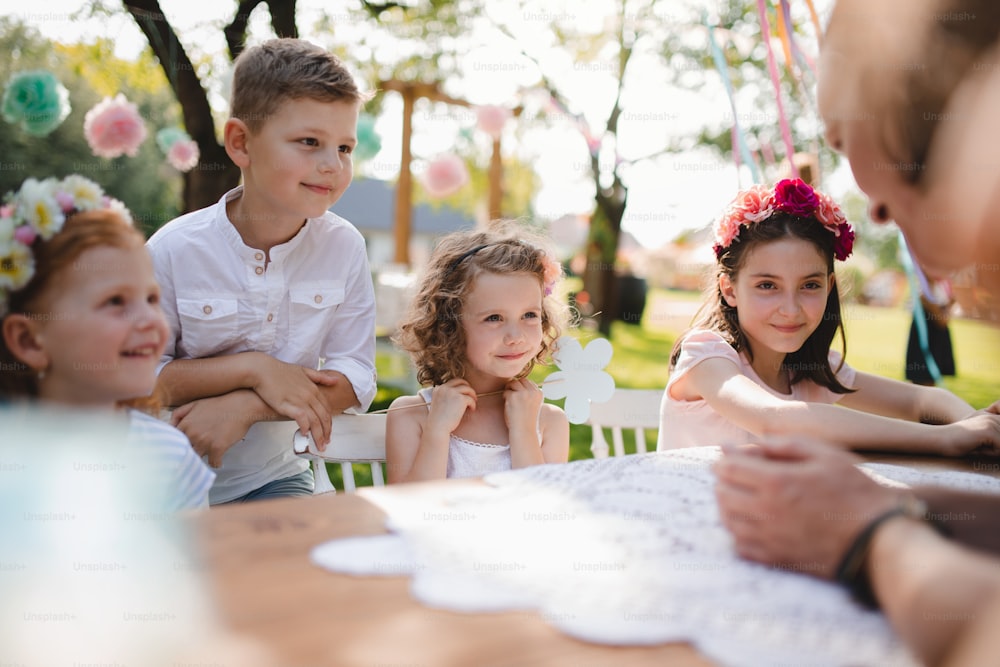 Kleine Kinder, die im Sommer auf einer Gartenparty im Freien am Tisch sitzen und sich unterhalten.