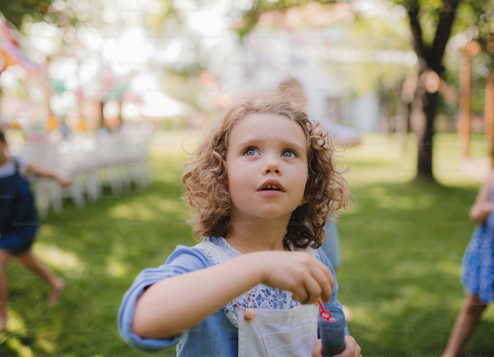 Small girl blowing bubbles outdoors in garden in summer, birthday celebration concept.