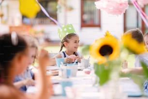 Group of small children sitting at the table outdoors on garden party in summer, eating.