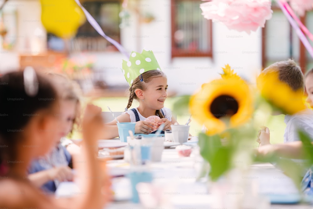 Gruppe von kleinen Kindern sitzen am Tisch im Freien auf Gartenparty im Sommer, essen.