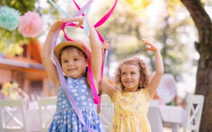 Small girls playing outdoors in garden in summer, a birthday celebration concept.