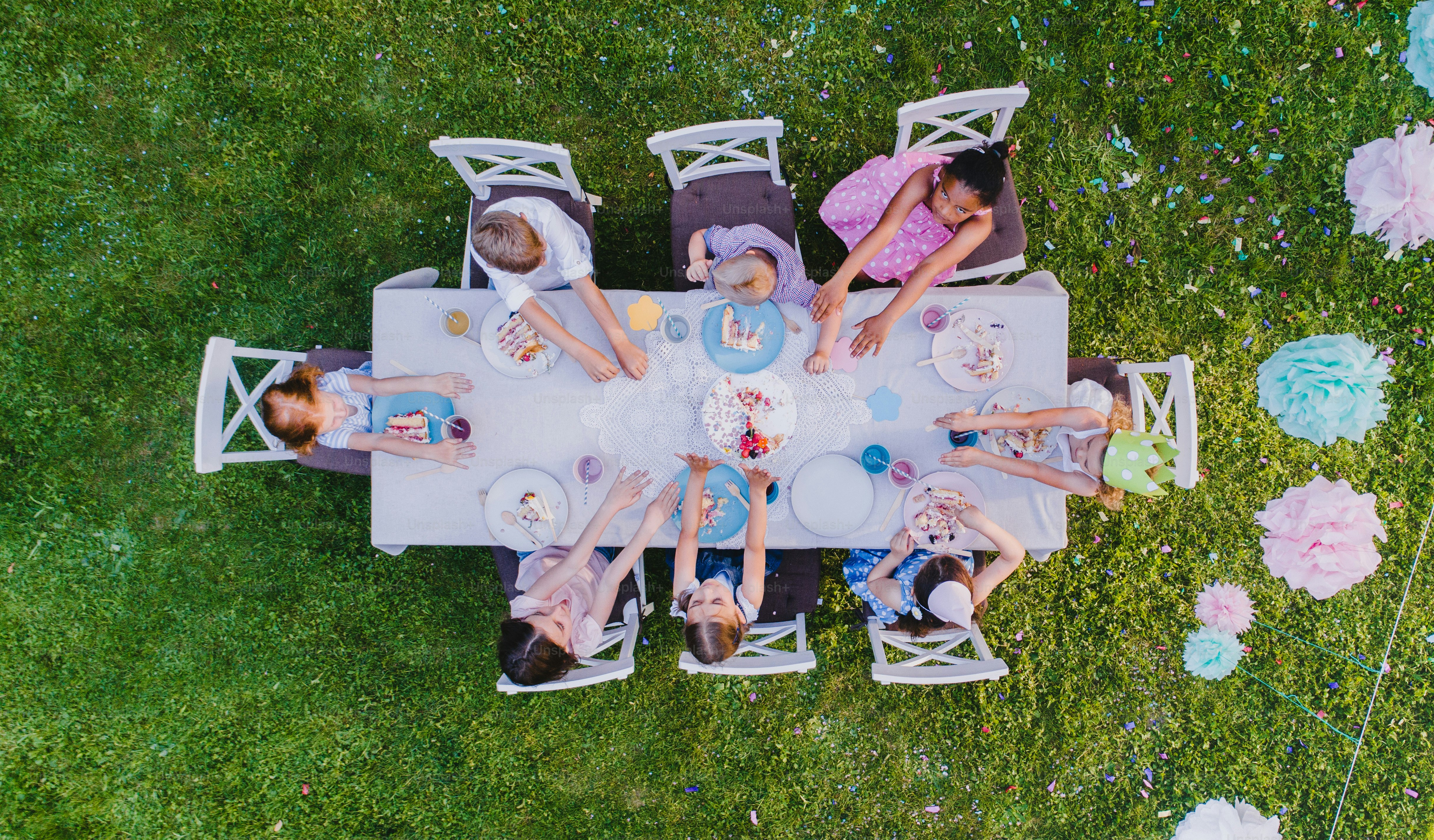 Top view of small children sitting at the table outdoors on garden party, eating cake.