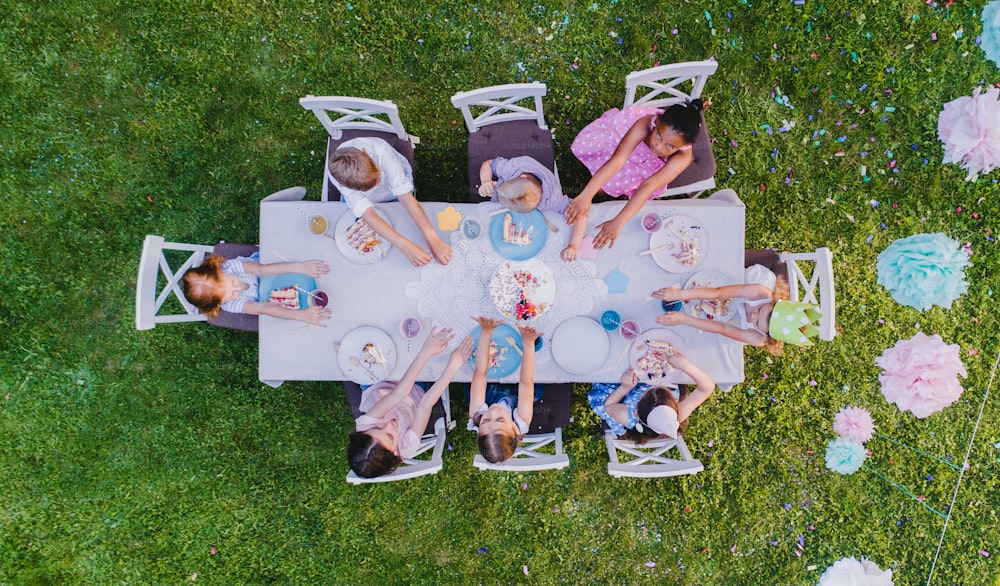 Top view of small children sitting at the table outdoors on garden party, eating cake.
