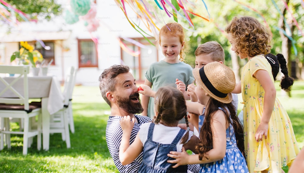 Ein Mann mit kleinen Kindern, der im Sommer draußen im Garten auf dem Boden sitzt und spielt.