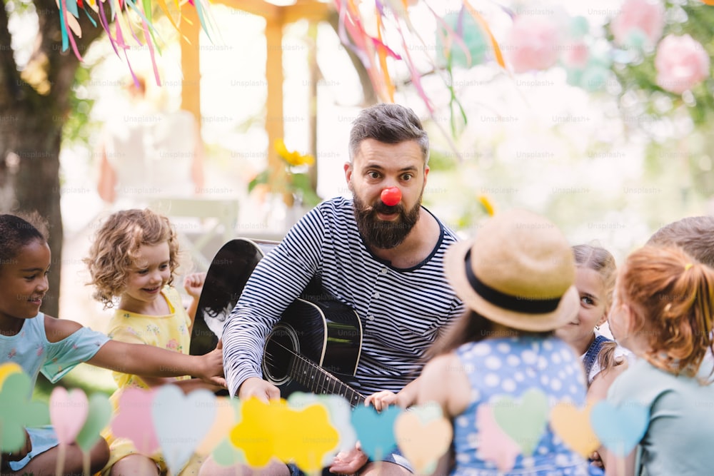 Ein Mann mit kleinen Kindern, der im Sommer draußen im Garten auf dem Boden sitzt und Gitarre spielt.