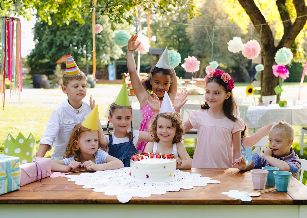 Down syndrome child with friends on birthday party outdoors in garden in summer.