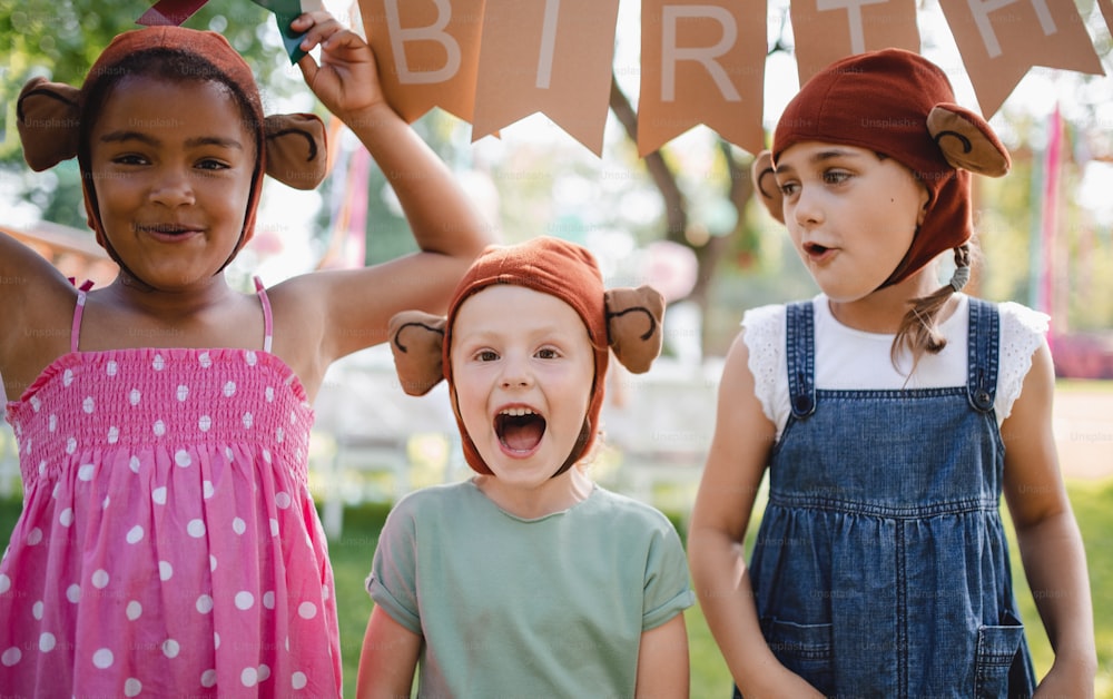 Crianças pequenas com máscaras em pé ao ar livre no jardim no verão, brincando. Um conceito de celebração.