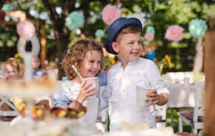 Small children standing outdoors in garden in summer, holding drinks. A celebration concept.