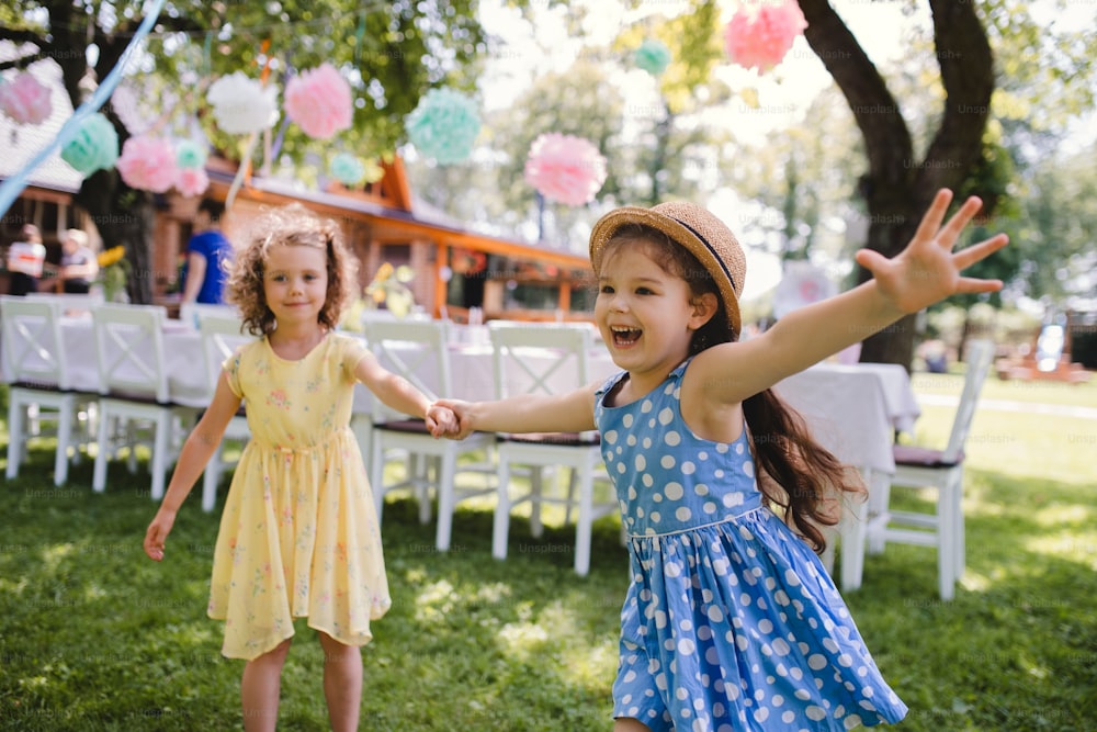 Small girls running outdoors in garden in summer, a birthday celebration concept.