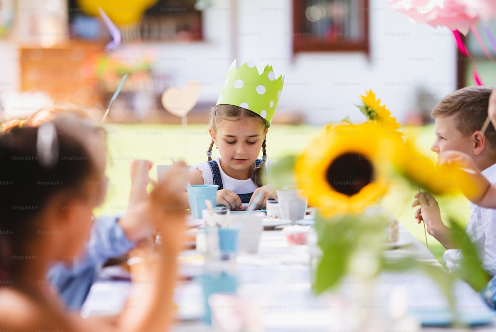 Grupo de niños pequeños sentados a la mesa al aire libre en la fiesta del jardín en verano, comiendo.