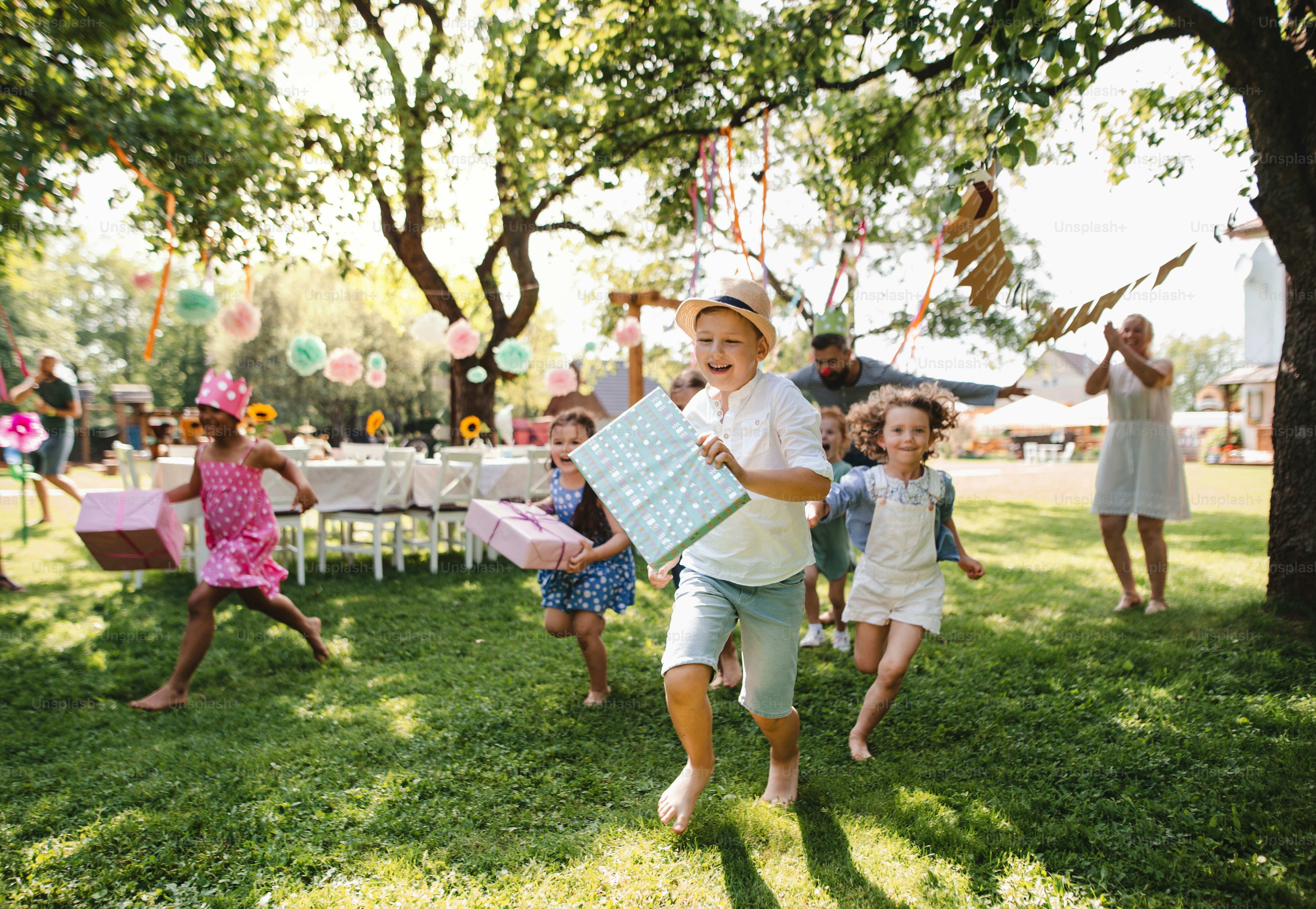 Small children ruunning with present outdoors in garden on birthday party, playing