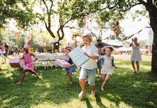 Small children ruunning with present outdoors in garden on birthday party, playing.