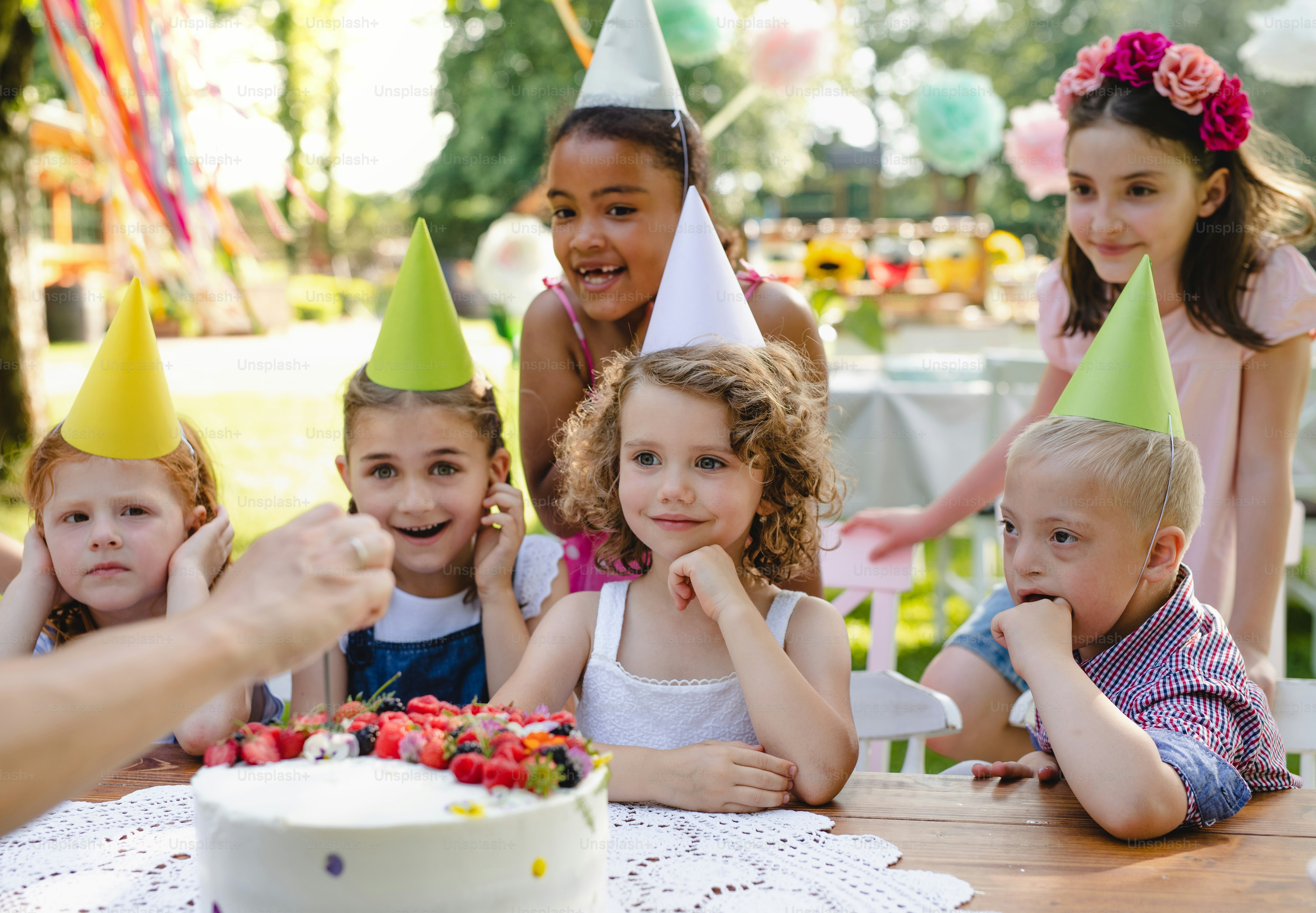 Down syndrome child with friends on birthday party outdoors in garden in summer.