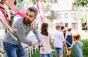 Man with group of kids on birthday party playing outdoors in garden in summer, celebration concept.
