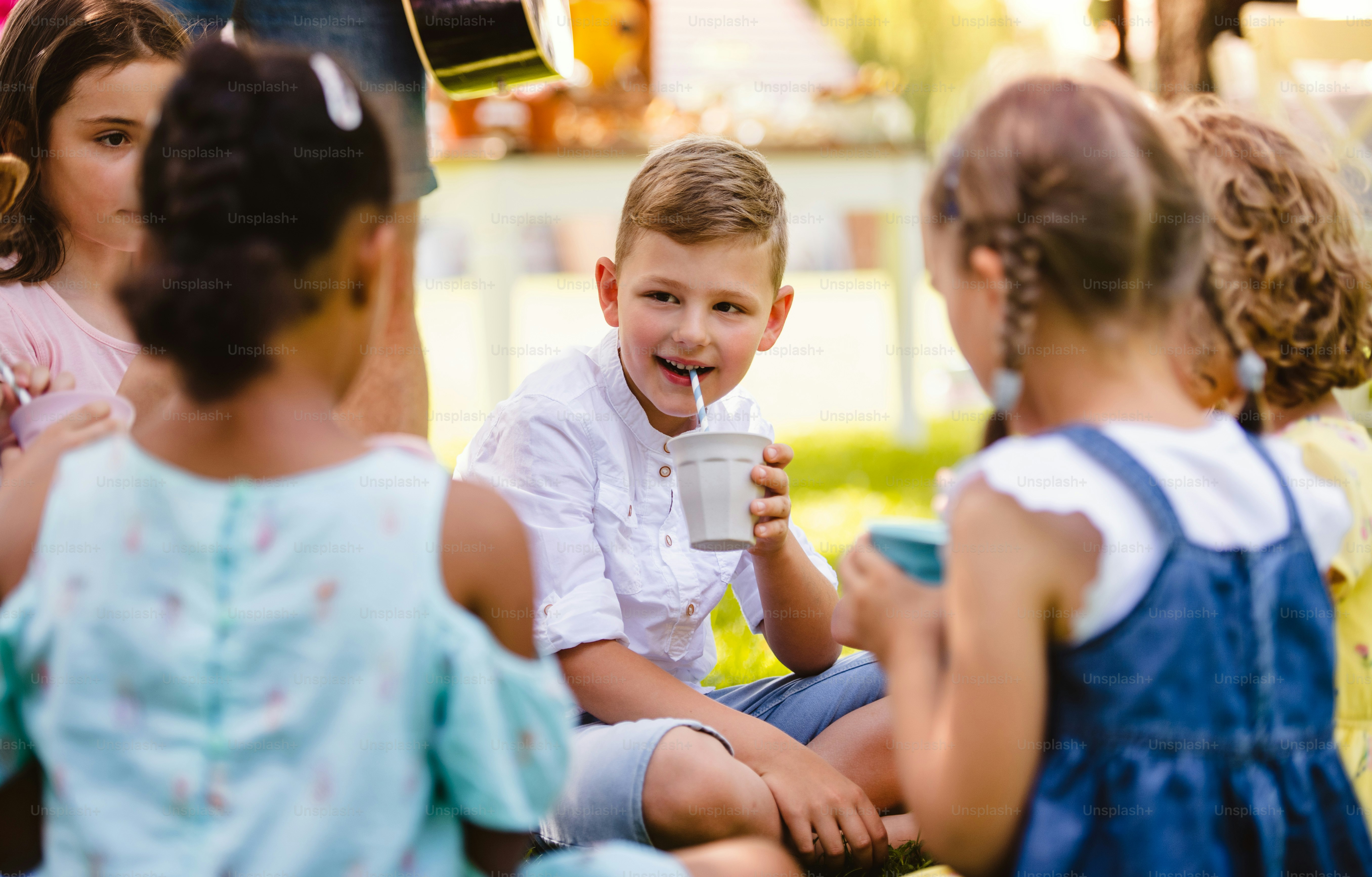 Kleine Kinder sitzen im Sommer im Garten auf dem Boden und trinken. Ein Festkonzept.