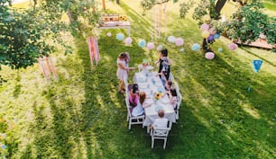 High angle view of small children sitting at the table outdoors on garden party in summer.