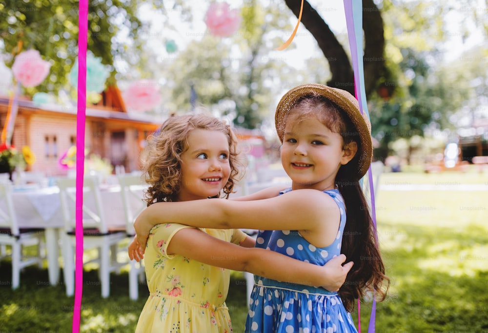 Small girls hugging outdoors in garden in summer, a birthday celebration concept.