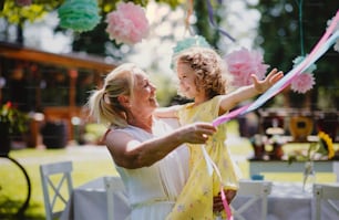 Grandmother holding small girll outdoors on garden party in summer, celebration concept.
