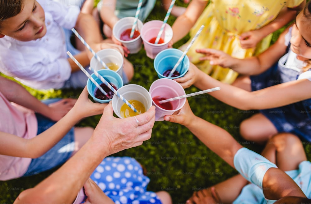 Mittelteil von kleinen Kindern, die im Sommer im Freien im Garten auf dem Boden sitzen und trinken. Ein Festkonzept.