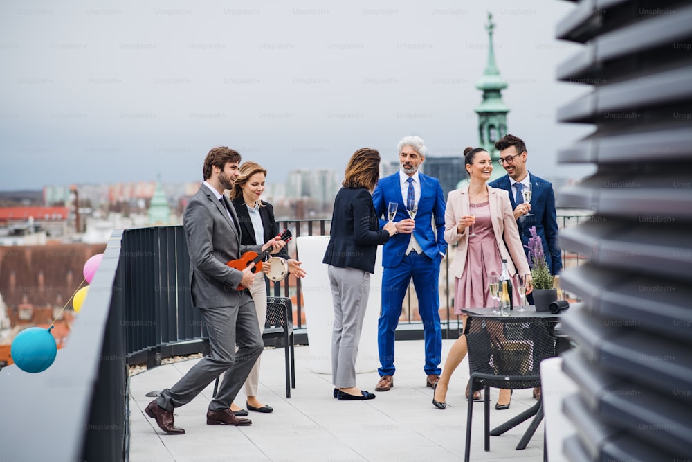 Eine große Gruppe von fröhlichen Geschäftsleuten, die eine Party im Freien auf der Dachterrasse in der Stadt veranstalten.