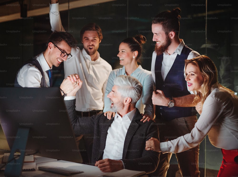 Un gruppo di uomini d'affari con computer in un ufficio di sera o di notte, esprimendo eccitazione.