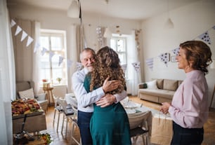 Young woman greeting senior parents or grandparents on a indoor birthday or anniversary party.