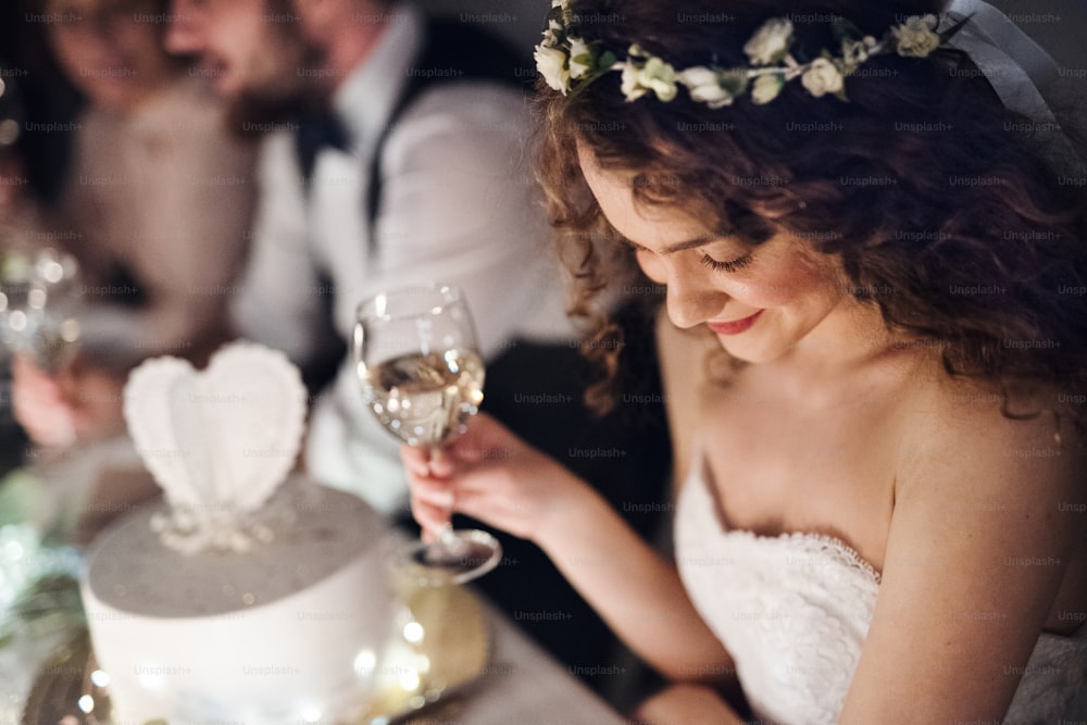 Un gros plan d’une jeune mariée assise à une table lors d’un mariage, tenant un verre de vin blanc.