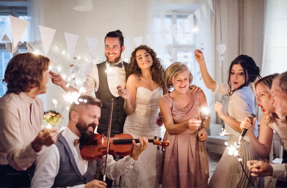 Eine junge, fröhliche Braut, ein Bräutigam und andere Gäste tanzen, singen und spielen Geige auf einer Hochzeitsfeier.