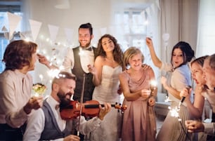 Uma jovem noiva alegre, noivo e outros convidados dançando, cantando e tocando violino em uma recepção de casamento.