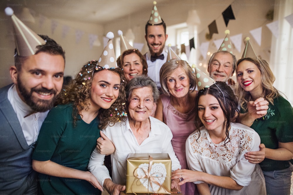 Un retrato de una familia multigeneracional con regalos de pie en el interior en una fiesta de cumpleaños.