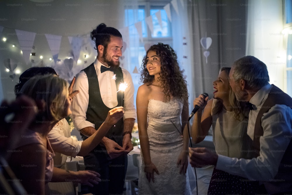 Uma jovem noiva e noivo alegres com outros convidados dançando e cantando em uma recepção de casamento.