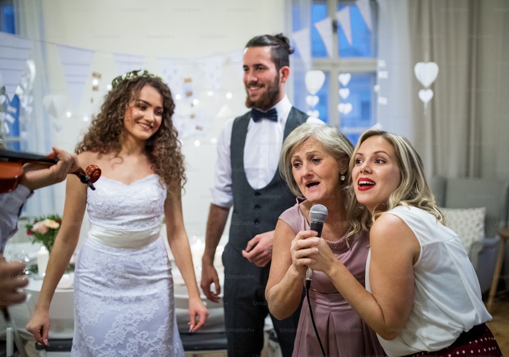 Una joven y alegre novia y novio con otros invitados bailando y cantando en una recepción de boda.