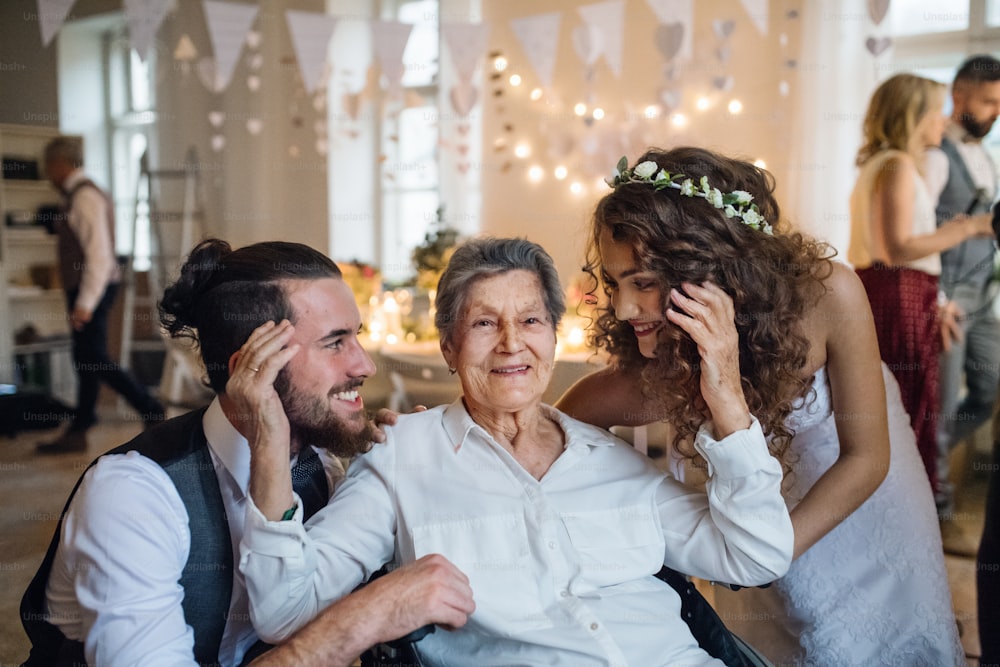 Ein junges Brautpaar mit Großmutter auf einer Hochzeitsfeier, posiert für ein Foto.