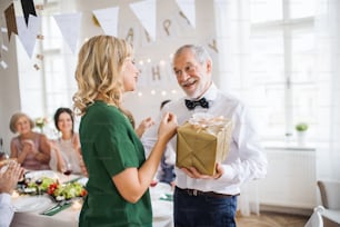 Beautiful young woman giving a gift to her father or grandfather on indoor party.