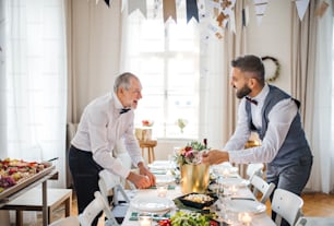 Two handsome men with bows setting a table for an indoor party, talking.
