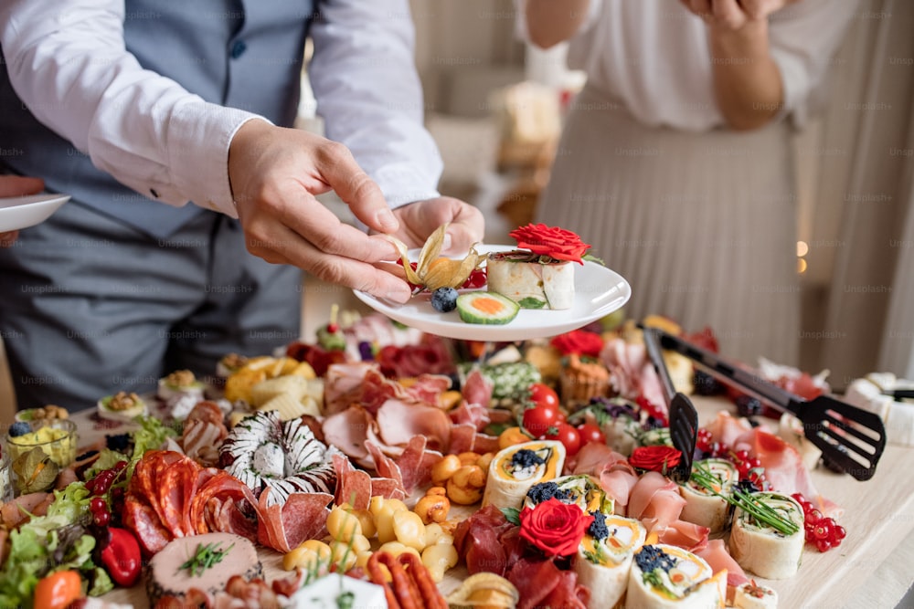 Sección media de un hombre poniendo comida en un plato en una fiesta de cumpleaños familiar en el interior.