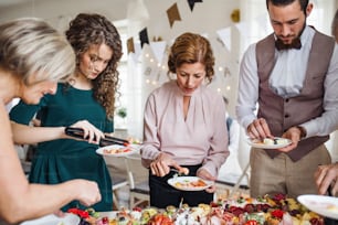 Une famille multigénérationnelle mettant de la nourriture dans des assiettes lors d’une fête d’anniversaire familiale à l’intérieur.