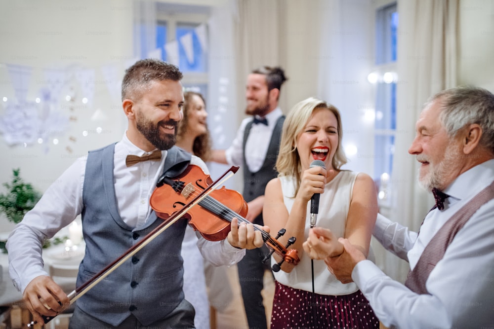 Eine junge, fröhliche Braut, ein Bräutigam und andere Gäste tanzen, singen und spielen Geige auf einer Hochzeitsfeier.