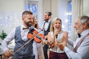 Una joven novia alegre, novio y otros invitados bailando, cantando y tocando el violín en una recepción de boda.